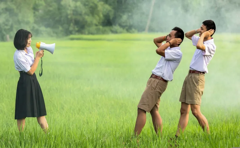 En tjej som gapar i en megafon och två killar som håller för öronen